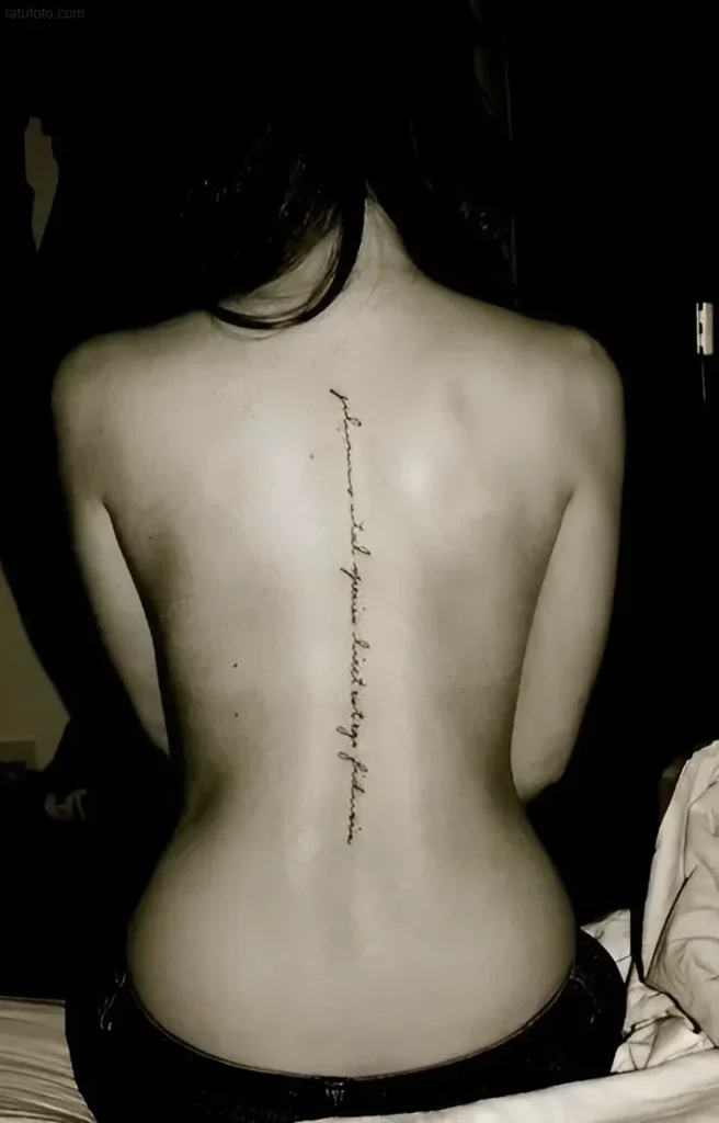 Photograph of a tattoo - a black inscription in a calligraphic font, located vertically along the spine of a slender girl.