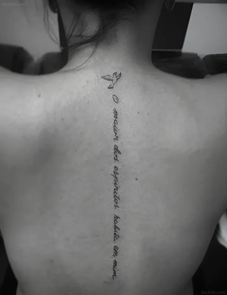 Tattoo photo: two flying birds and a Latin phrase, placed vertically along a girl's spine.
