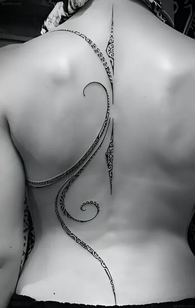 Black and white photo of a Maori-style tattoo running along the spine of a woman's back, with an emphasis on flowing lines and geometric patterns.