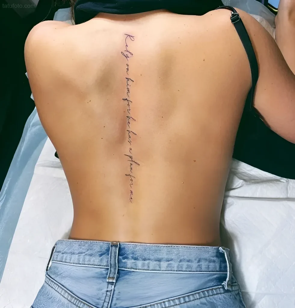 Photograph of a tattoo along a girl's spine: a thin inscription in a calligraphic font.