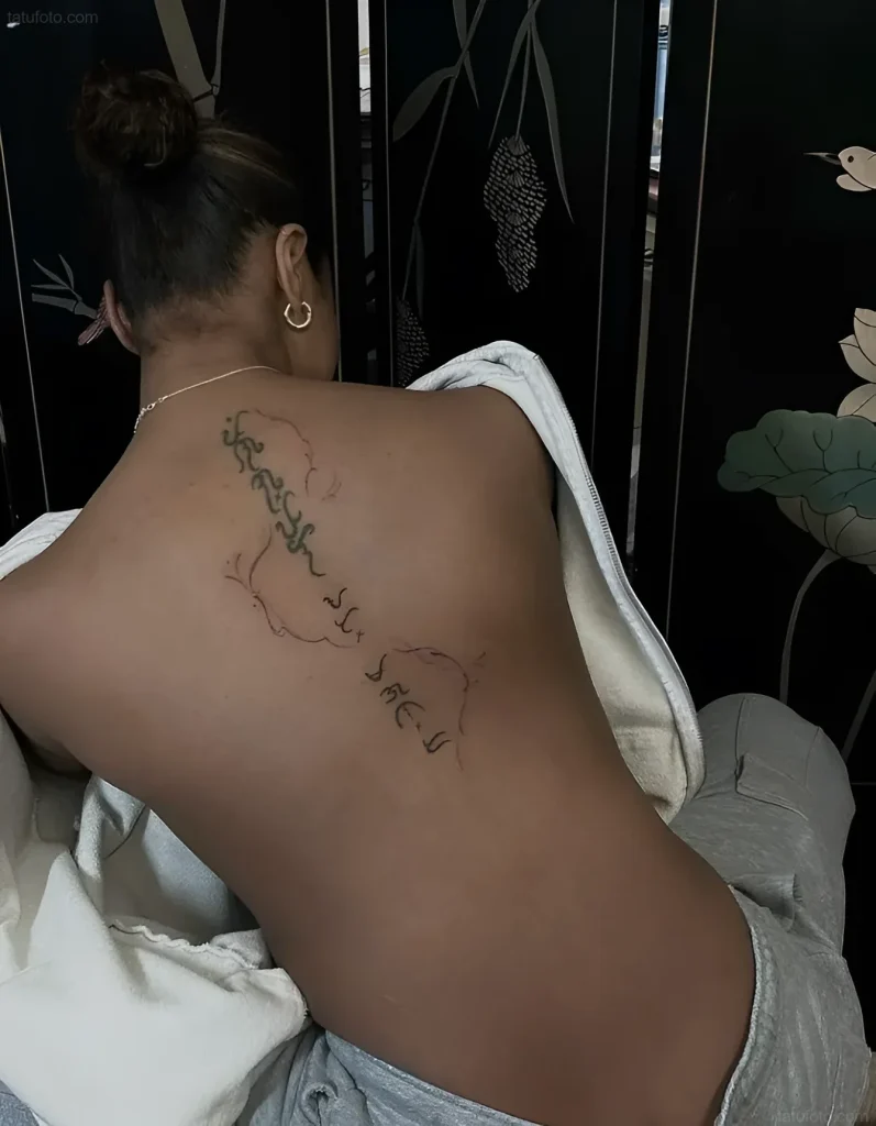 Tattoo photo on a girl's back: a thin line of hieroglyphs and clouds, located along the spine.