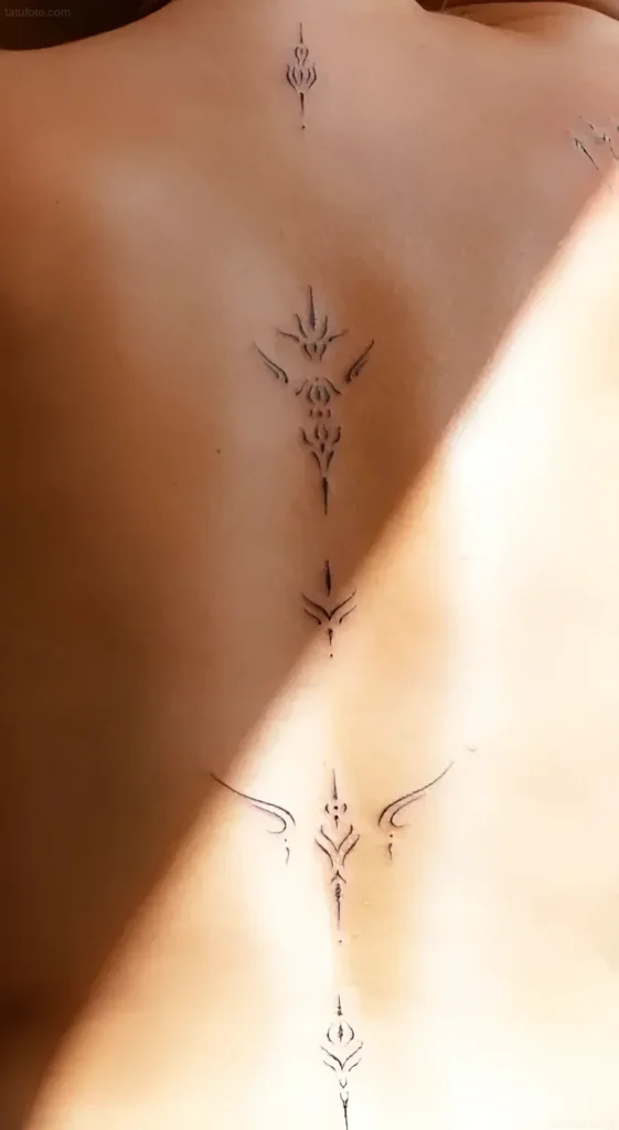 Tattoo photo: a thin black ornament along the spine, woman's back, minimalism, tattoo design