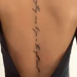 Фото татуировки: Надпись 'Be patient everything comes to you in the right moment' вдоль женского позвоночника, выполненная тонкой линией.