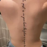 Фотография татуировки вдоль позвоночника с фразой 'The past is in your head, the future is in your hands', выполненной изящным шрифтом.