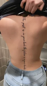 Фотография татуировки вдоль позвоночника с фразой 'The past is in your head, the future is in your hands', выполненной изящным шрифтом.