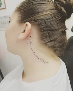 Фото татуировки за ухом: изящная надпись 'Go where the stars take you' и россыпь маленьких звезд на шее девушки