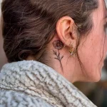 Фото татуировки: маленькая тату ромашки в технике тонкой линии за ухом девушки, вид сбоку.
