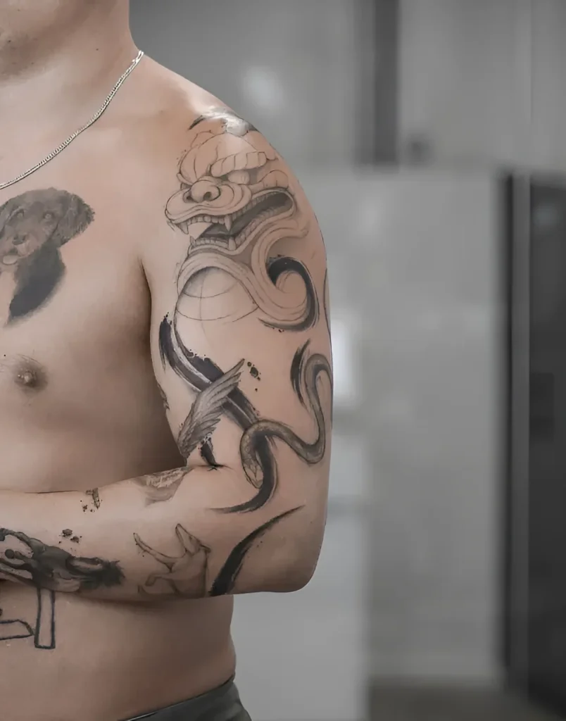 Man's shoulder with a black and white graphic tattoo: a fierce dragon wrapping around a winged bird.