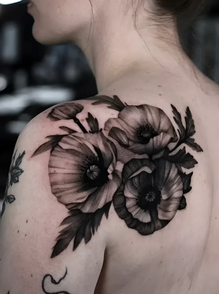 Black and white tattoo of poppies on the shoulder blade, done in realistic graphics with detailed petals and buds.