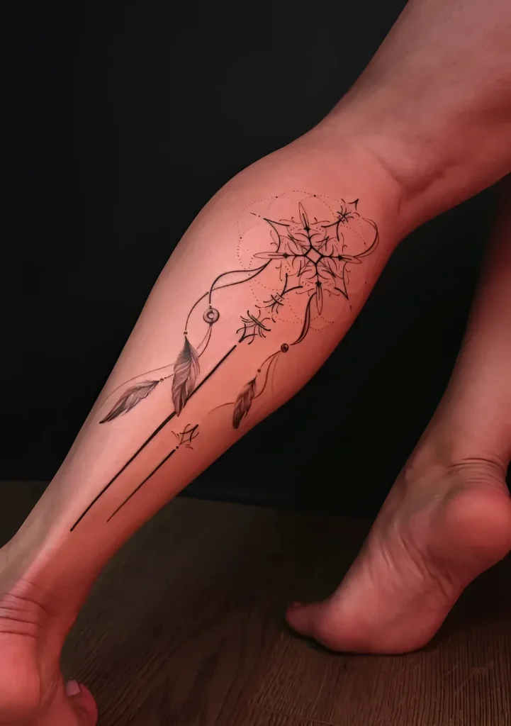 Black and white dreamcatcher tattoo with feathers, done on a girl's calf in a graphic style.