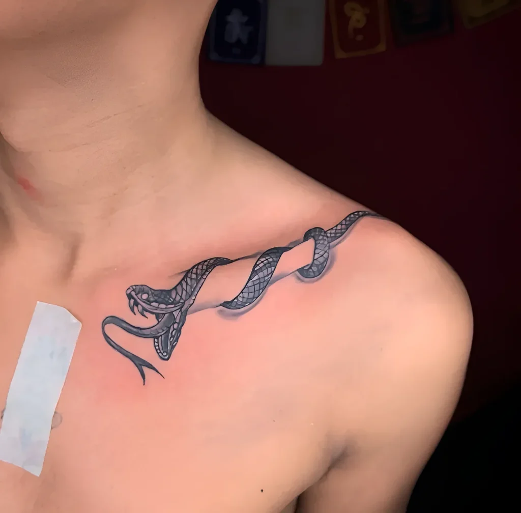 Photo of a snake tattoo wrapping around the collarbone, done in black graphic technique with smooth tonal transitions.