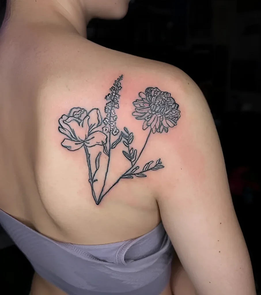 Black and white tattoo on the shoulder blade: blooming peonies and a lavender stem, done in a graphic style.