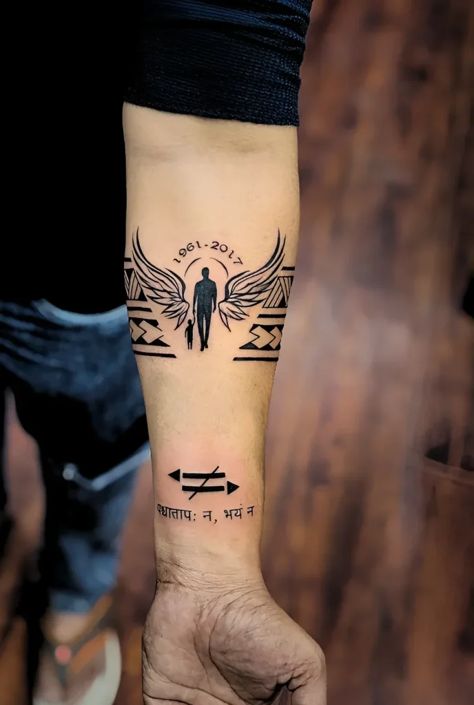 Black and white forearm tattoo depicting the silhouette of a person with wings, accompanied by the silhouette of a child, and the dates '1961-2017', as well as an inscription in Sanskrit.