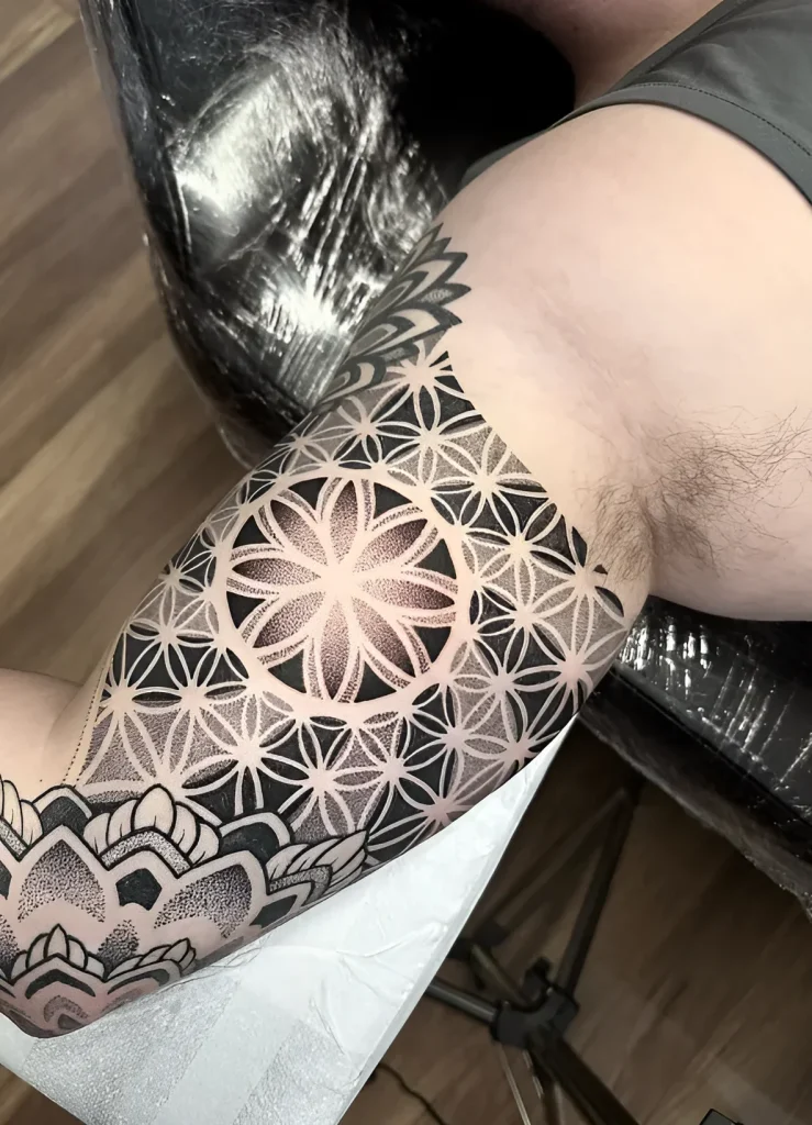 Photo de tatouage sur le biceps : gros plan d'un motif géométrique de style Dotwork représentant la Fleur de Vie, réalisé en noir et blanc.