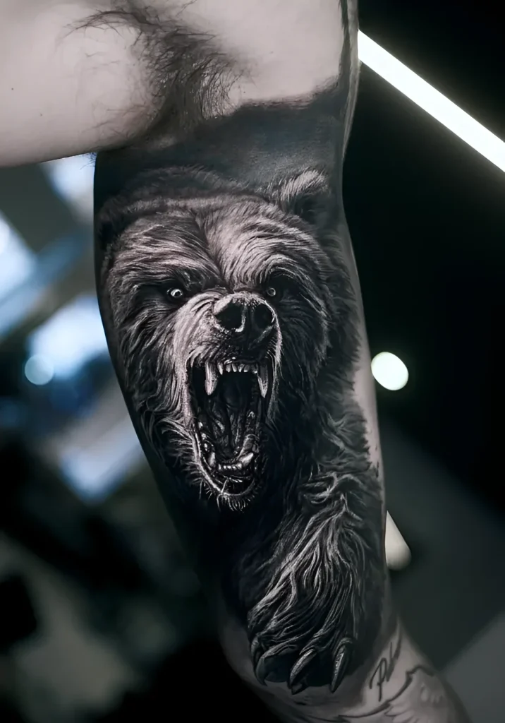 Photo de tatouage sur le biceps : image réaliste d'un ours rugissant en tons noir et gris, montrant les détails de la fourrure et des griffes.