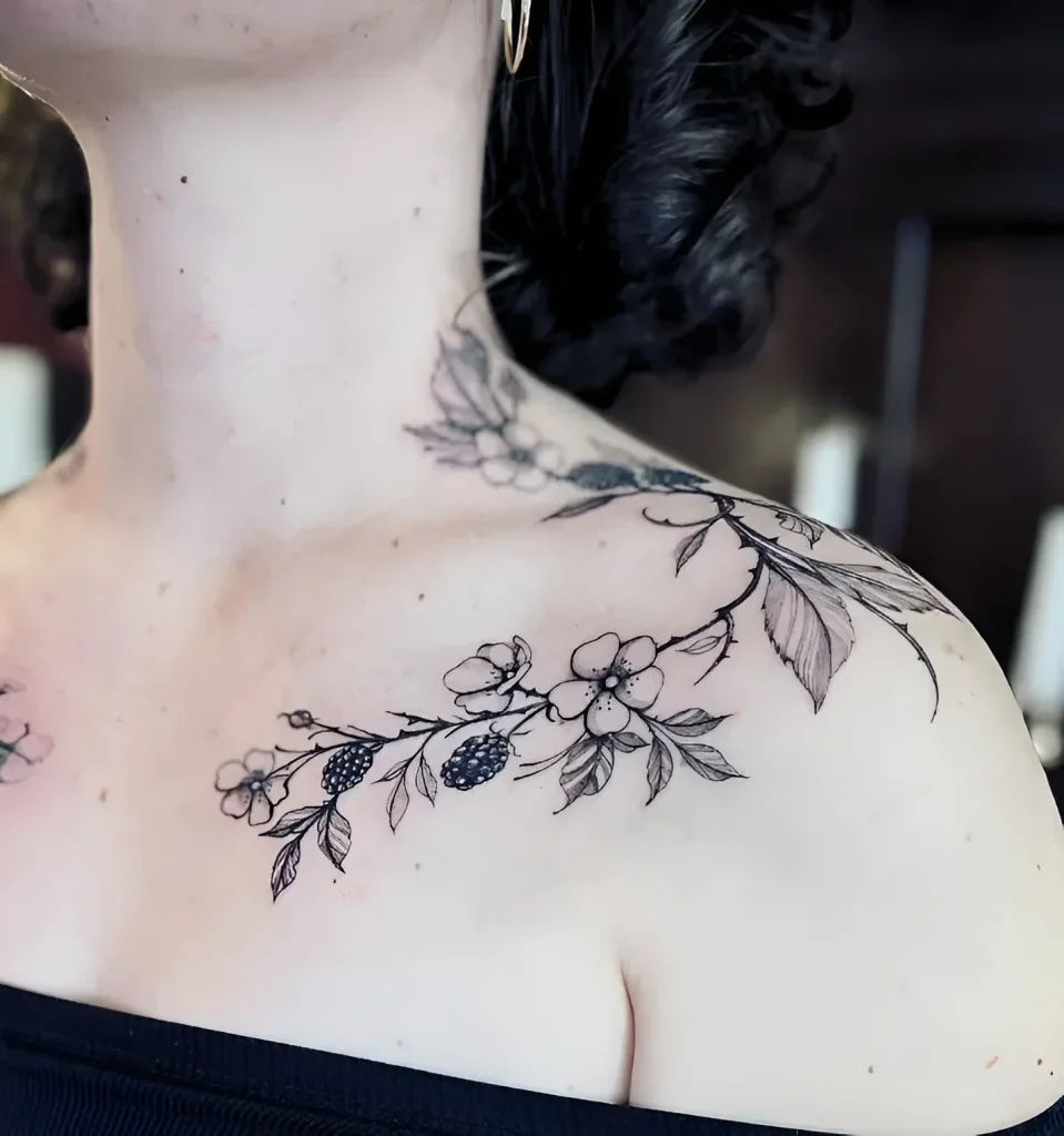 Black and white tattoo of a blooming sakura branch, smoothly transitioning from the collarbone to the shoulder, with detailed flowers and leaves.