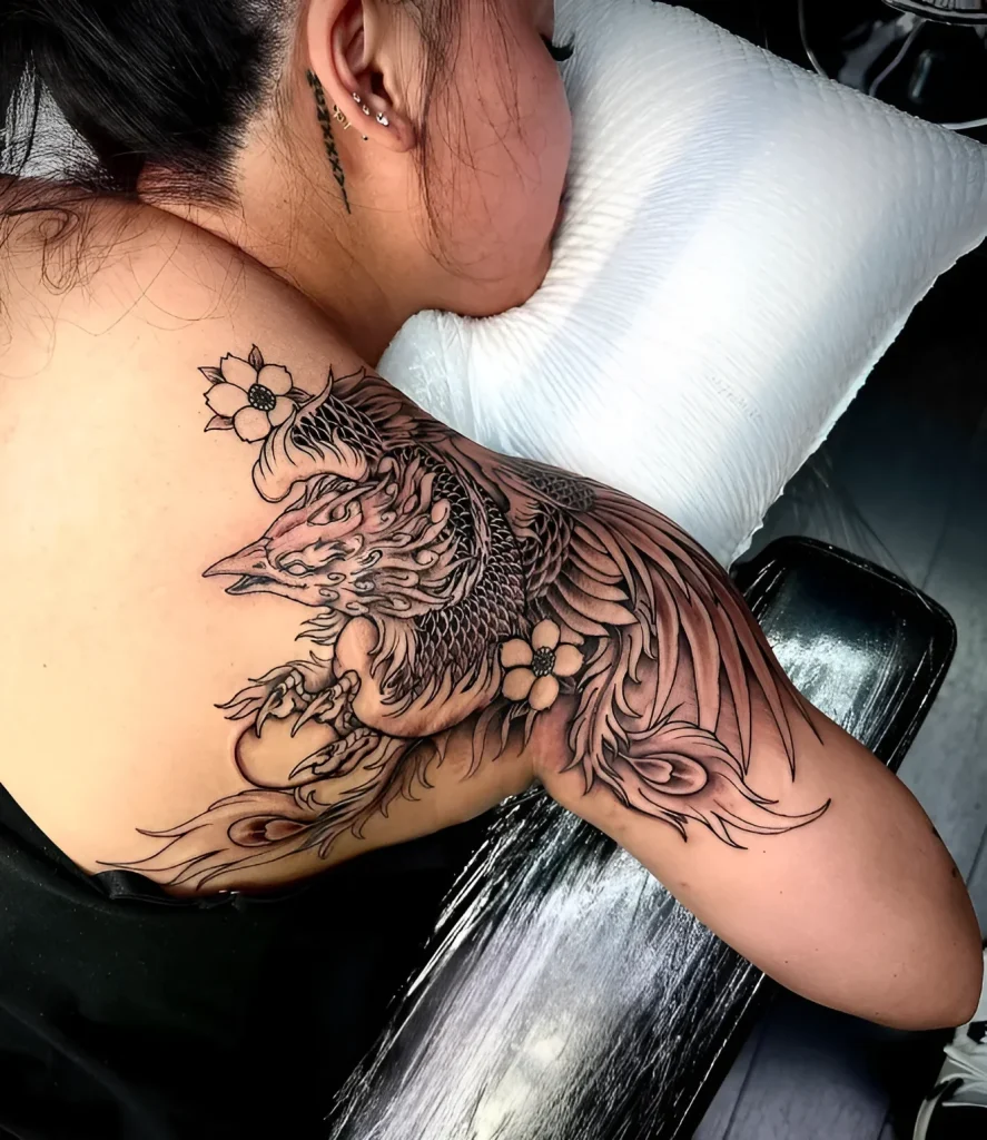 Black and white tattoo of a phoenix on a girl's shoulder blade, done in realistic graphic technique with elements of Japanese surrealism.