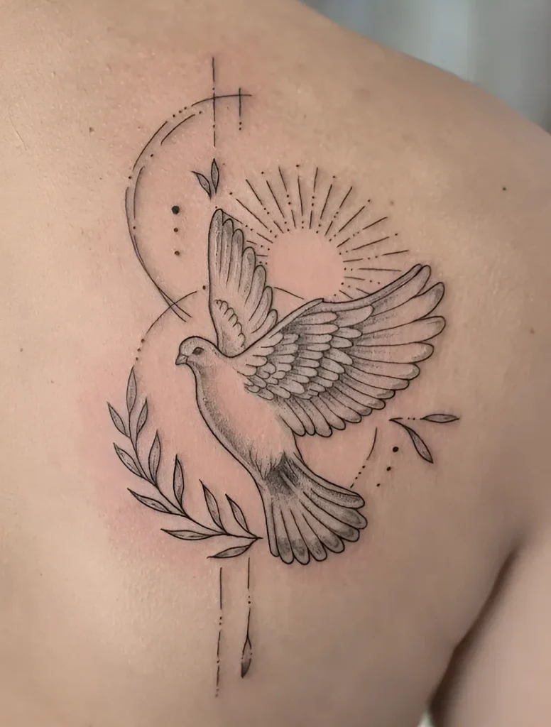 Black and white tattoo of a dove with spread wings on the shoulder blade, surrounded by rays of light and an olive branch.