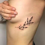 Черно-белая татуировка веточки с листьями на боку, под грудью, выполненная в технике лайнаворк
