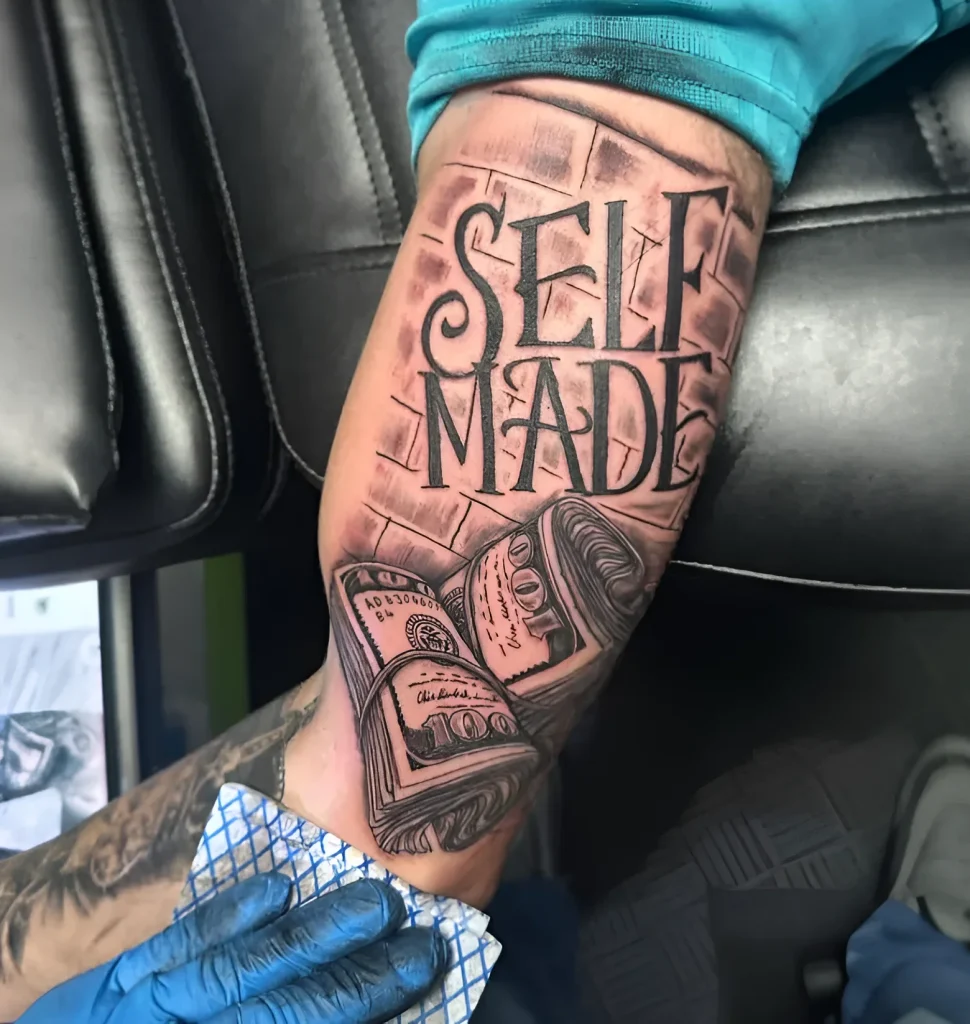 Tatouage noir et blanc sur le biceps d'un homme représentant des dollars froissés et l'inscription 'Self-Made', réalisé dans un style réaliste.
