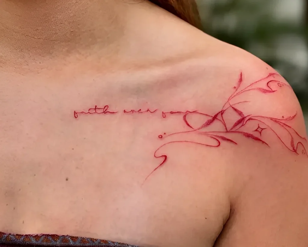 Close-up of a collarbone tattoo with the inscription 'Faith over fear' and an abstract floral ornament in soft pink tones.