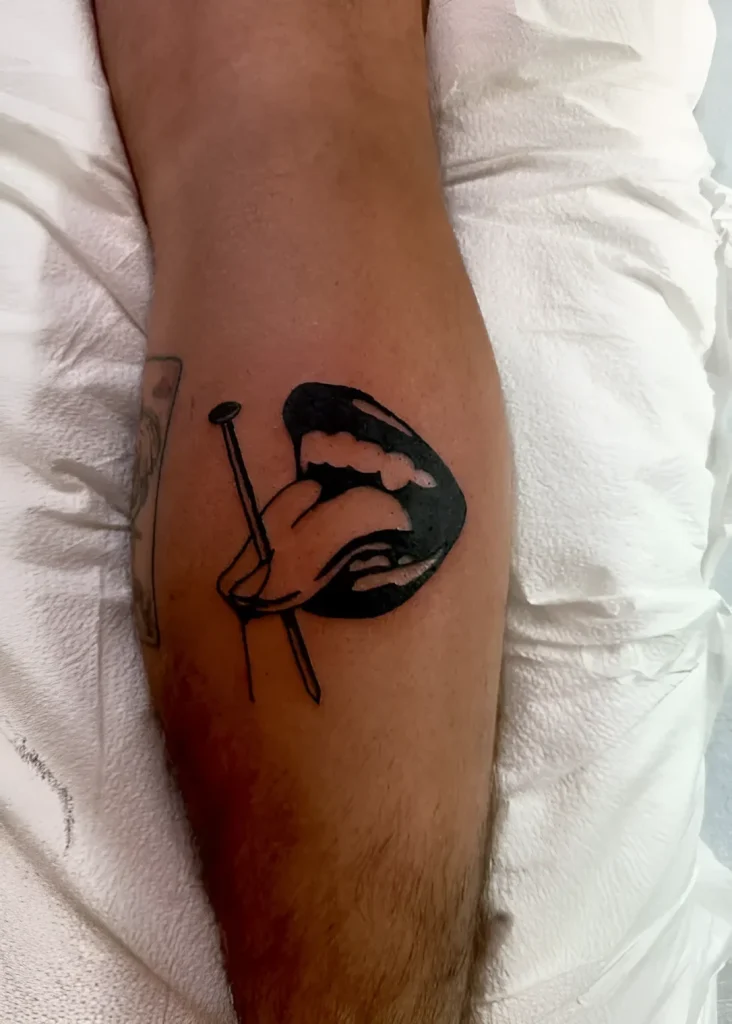 Black and white calf tattoo: stylized female lips holding two nails, minimalist design.