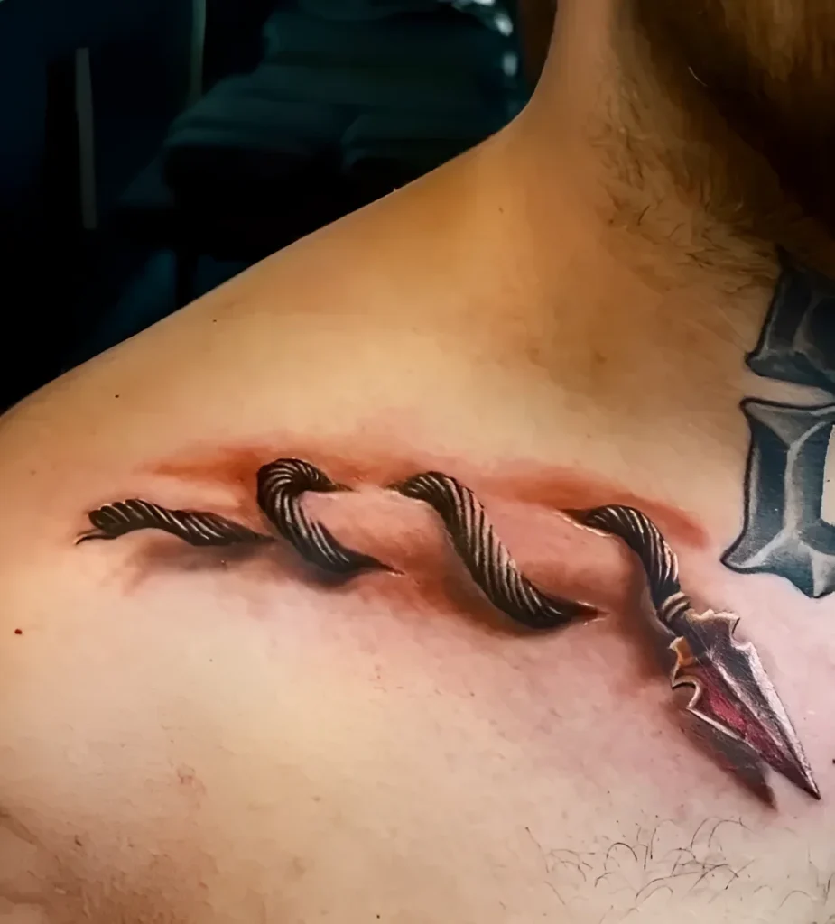 Realistic tattoo of an arrow piercing the skin on the collarbone, with detailed rendering of the fletching and arrowhead.