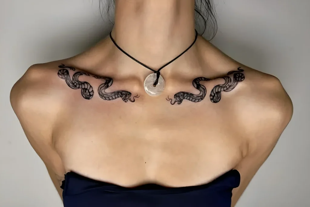 Black and white tattoo of two snakes, symmetrically placed on the girl's collarbones, with detailed scales and expressive heads.
