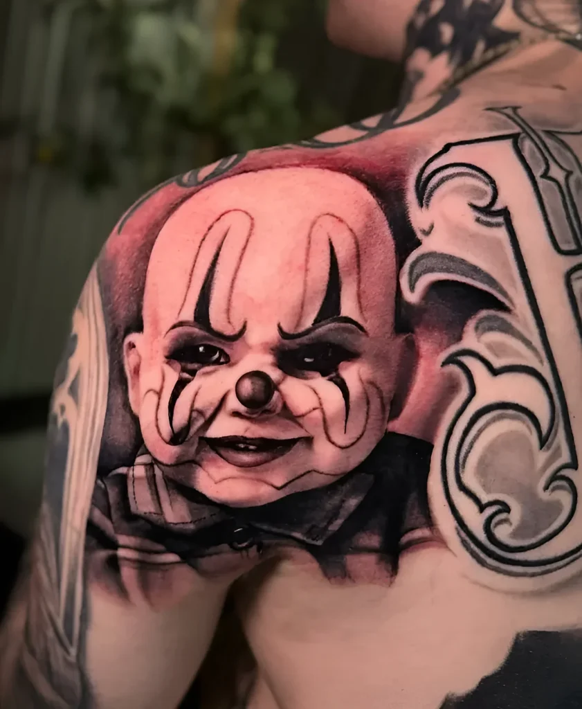 Black and grey realistic tattoo of a clown on a man's shoulder blade, with ornamental background elements.