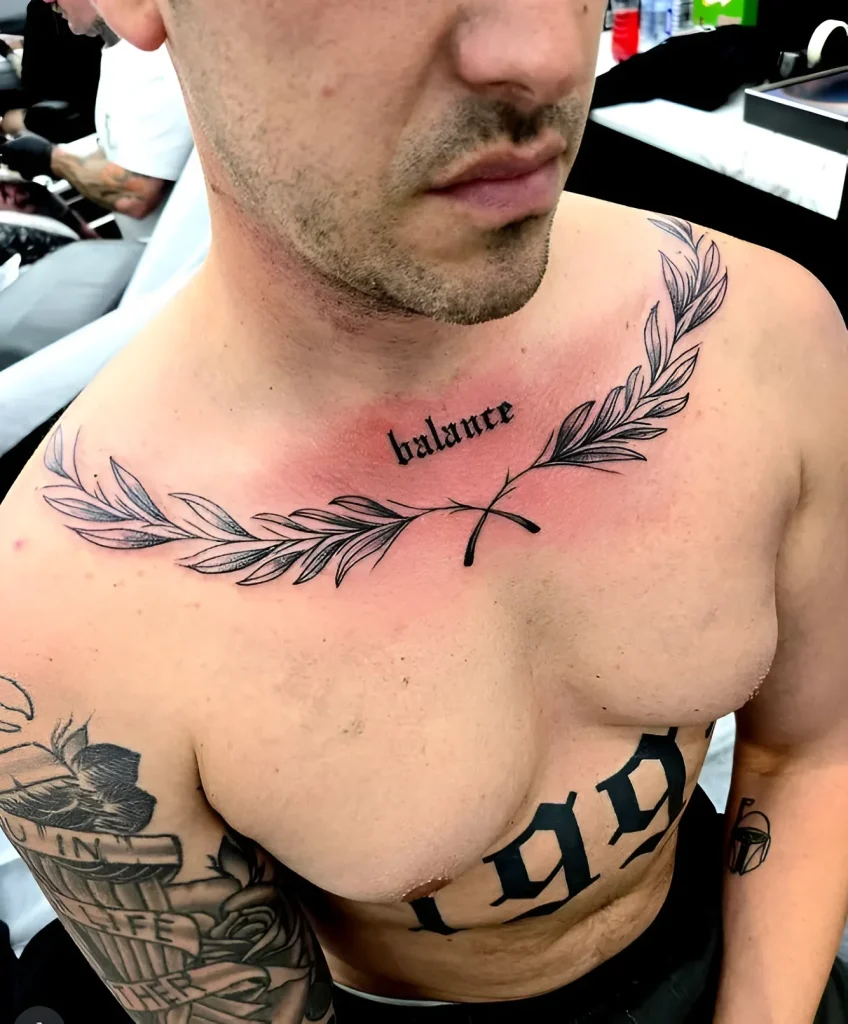 Men's collarbone tattoo: a thin laurel wreath with the inscription 'balance', done in linework technique.