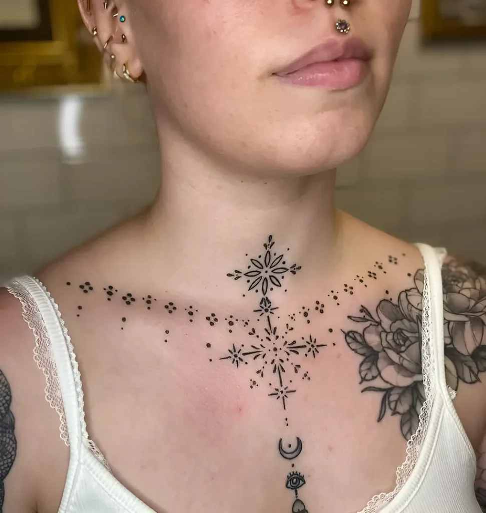 Black and white tattoo on a girl's collarbone, depicting falling stardust and a geometric flower, symbolizing beauty and inner strength.