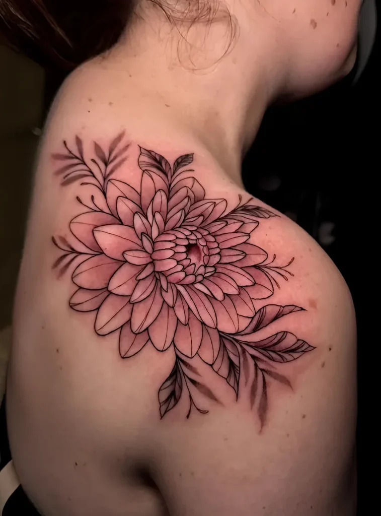 Black and white tattoo of a dahlia on the shoulder blade, done in linework technique with light shading of the flower's center.