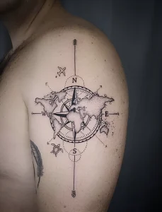 Мужская татуировка на плече: детализированный компас с контурами материков и морской черепахой, выполненная в технике лайнаворк.