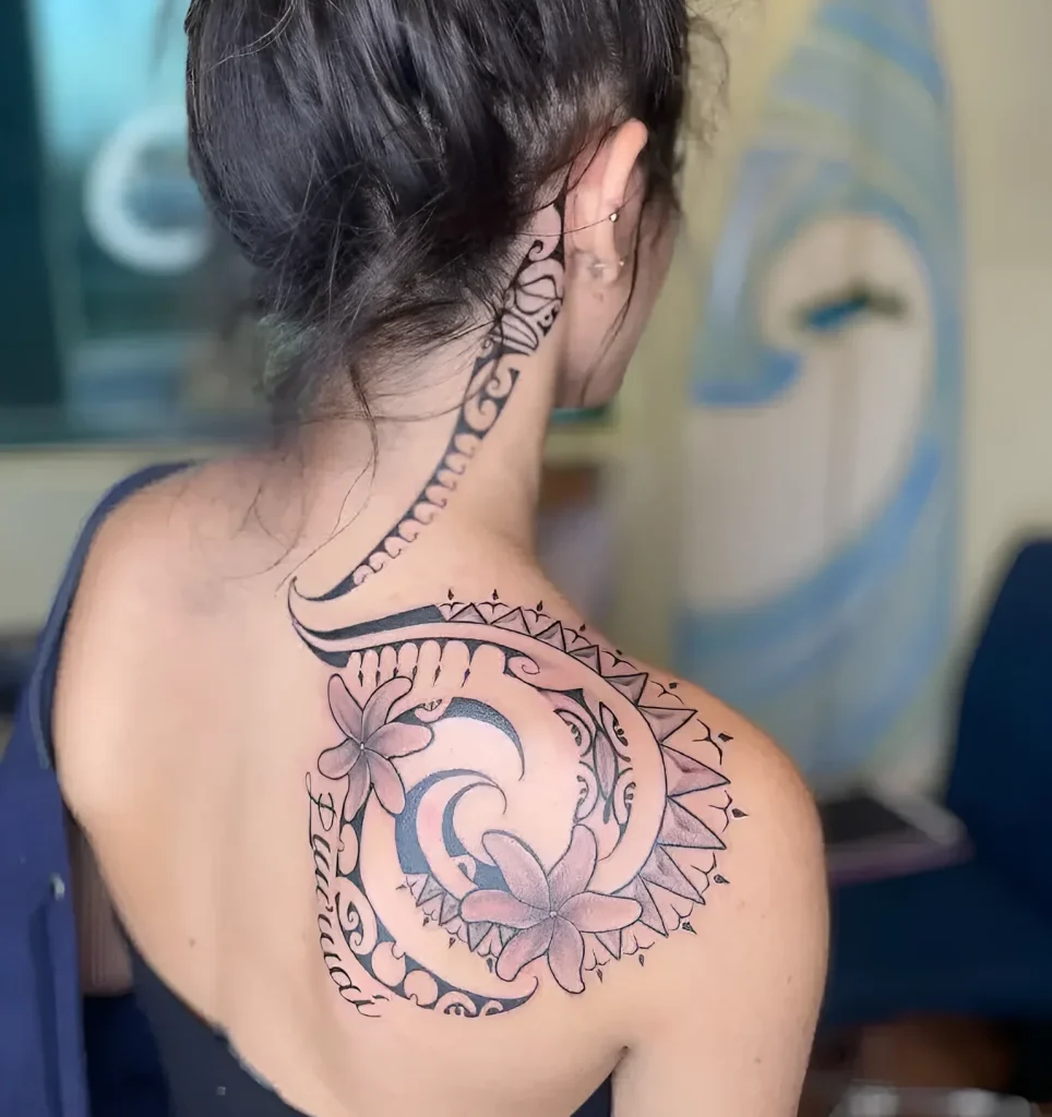 Female Polynesian style tattoo on the shoulder blade with images of the moon, waves, and flowers, done in black ink.