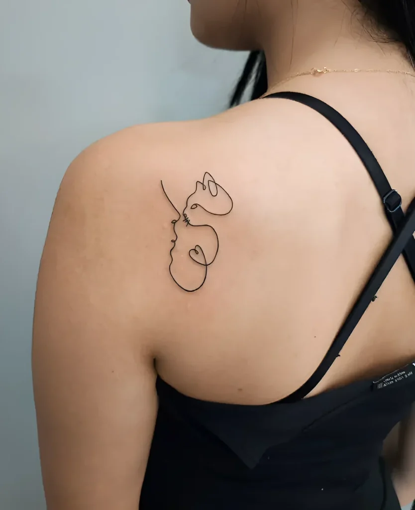Photo of a tattoo on the shoulder blade: a minimalist cat face done in a single line, on tanned female skin.