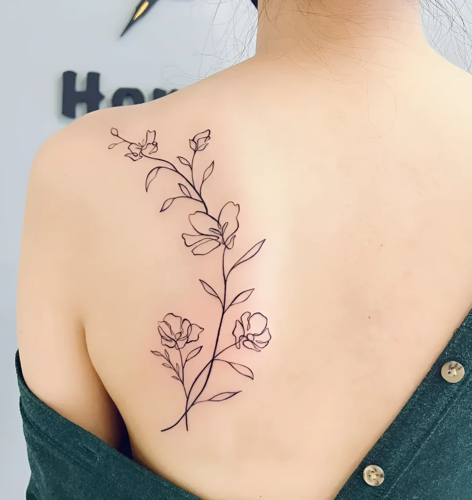 Photo of a tattoo on the shoulder blade: a thin black outline branch with blooming flowers, done in a minimalist style.