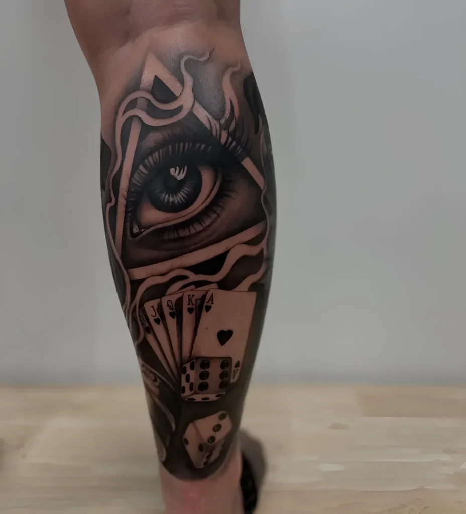 Black and white calf tattoo: realistic eye looking through cards and dice, done in blackwork technique.