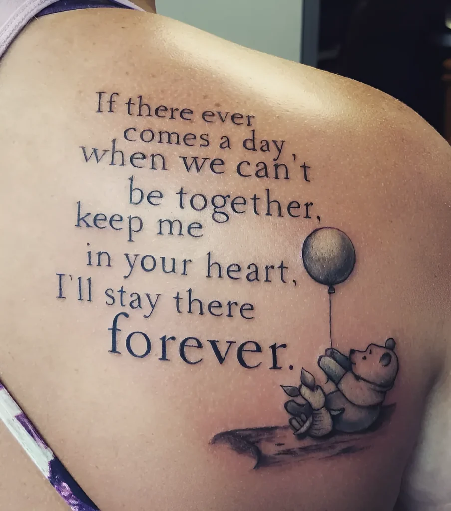 Black and grey tattoo on the shoulder blade: Winnie the Pooh lying on a cloud holding a balloon, with a quote in English around it.