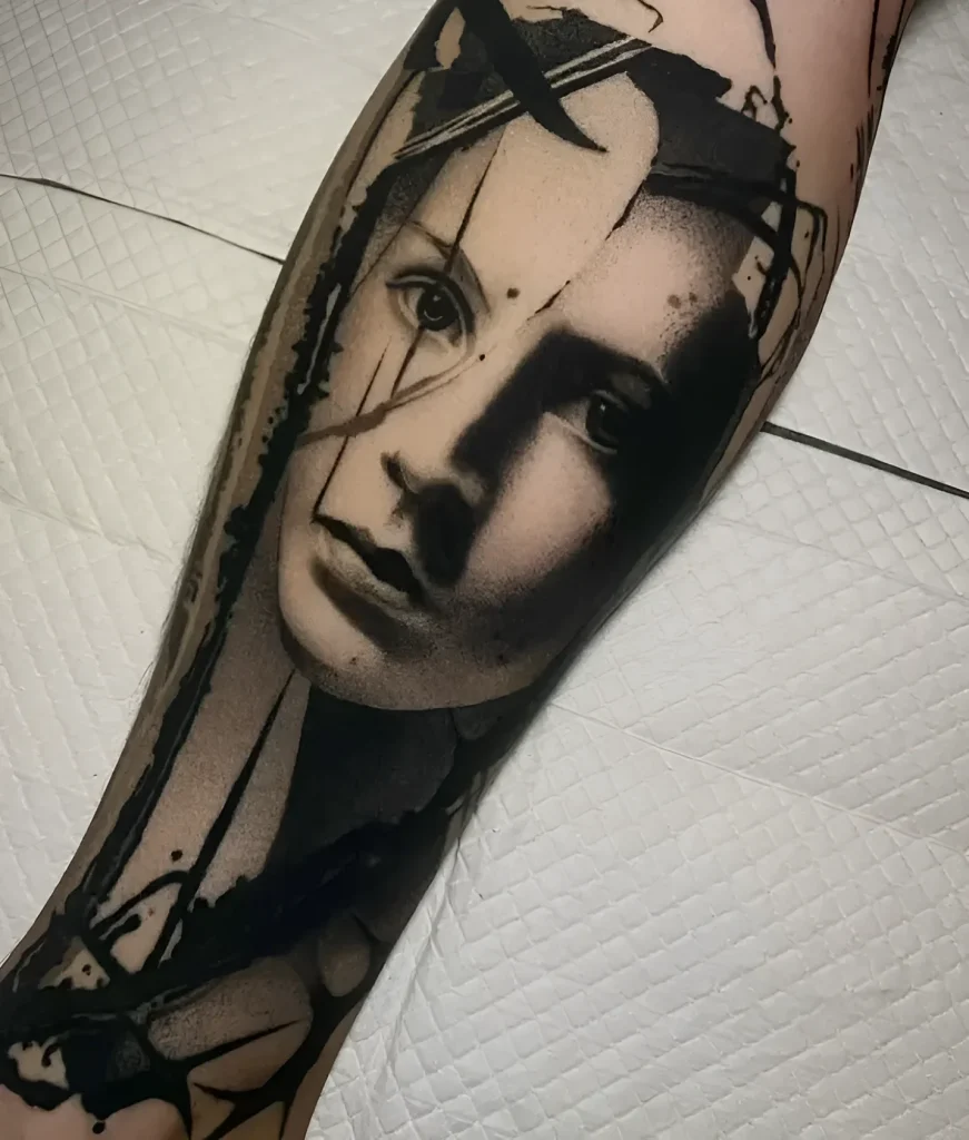Black and white calf tattoo portrait of a girl, done in realism style with graphic elements and a paint splatter effect.