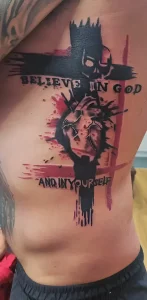 Фотография татуировки на боку мужчины: крест из шипов, сердце и надпись 'Believe in God and in Yourself' выполнены в технике блэкворк с элементами акварели.