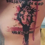 Фотография татуировки на боку мужчины: крест из шипов, сердце и надпись 'Believe in God and in Yourself' выполнены в технике блэкворк с элементами акварели.