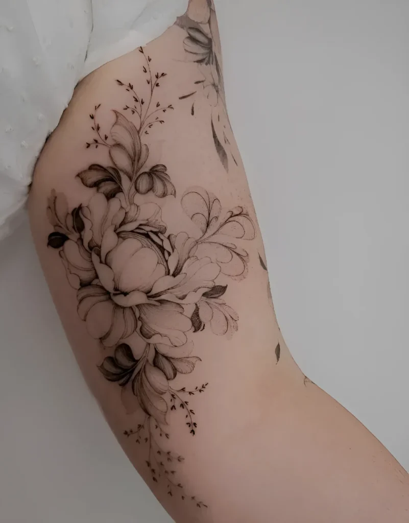 Tatouage noir et blanc sur le biceps représentant un bouquet luxuriant de pivoines et de brindilles avec de petites fleurs, réalisé dans un style d'illustration botanique.
