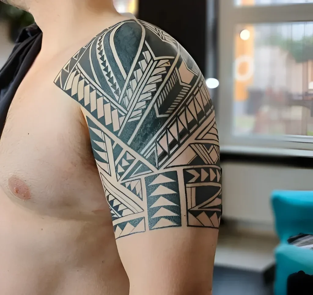 Man's shoulder adorned with a large Polynesian pattern tattoo in black tones, emphasizing the deltoid muscle.