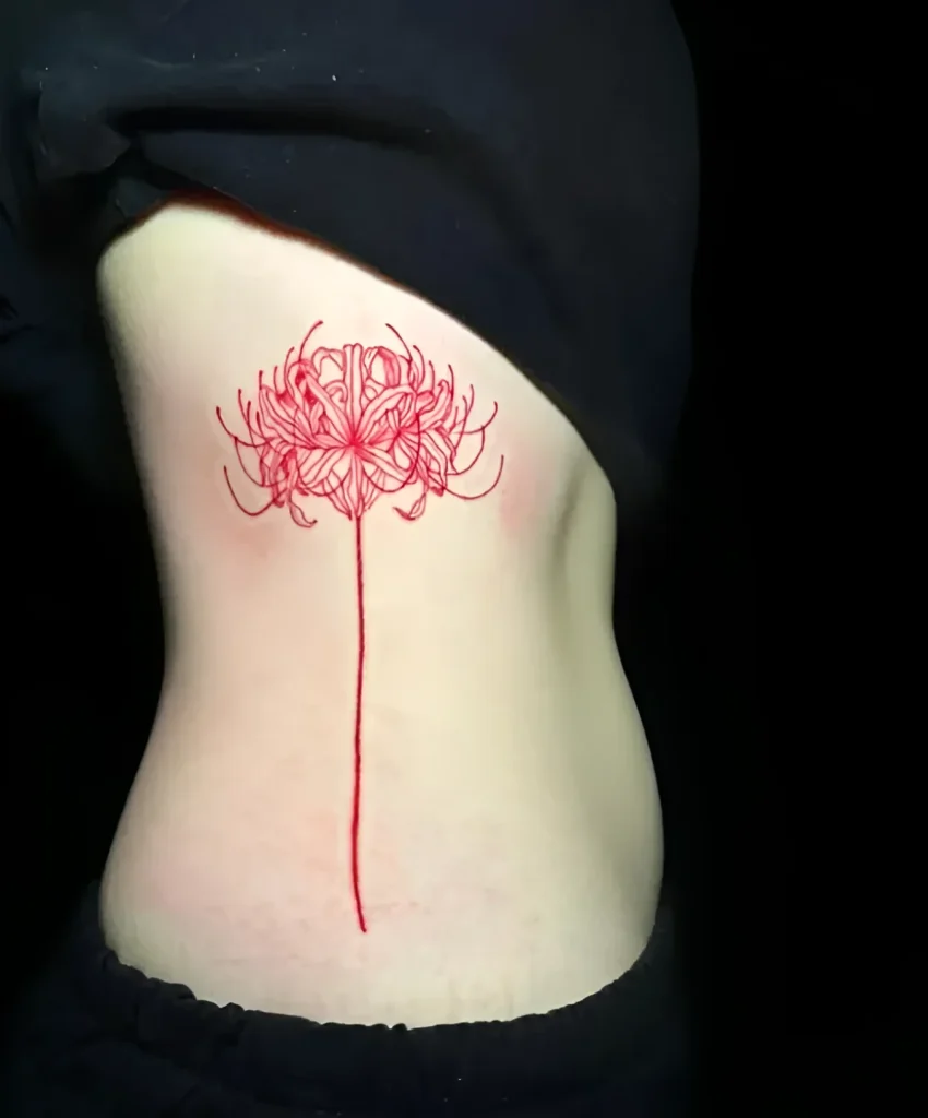 Gros plan d'un tatouage de lys araignée rouge, réalisé avec des lignes fines sur le flanc d'une jeune femme.