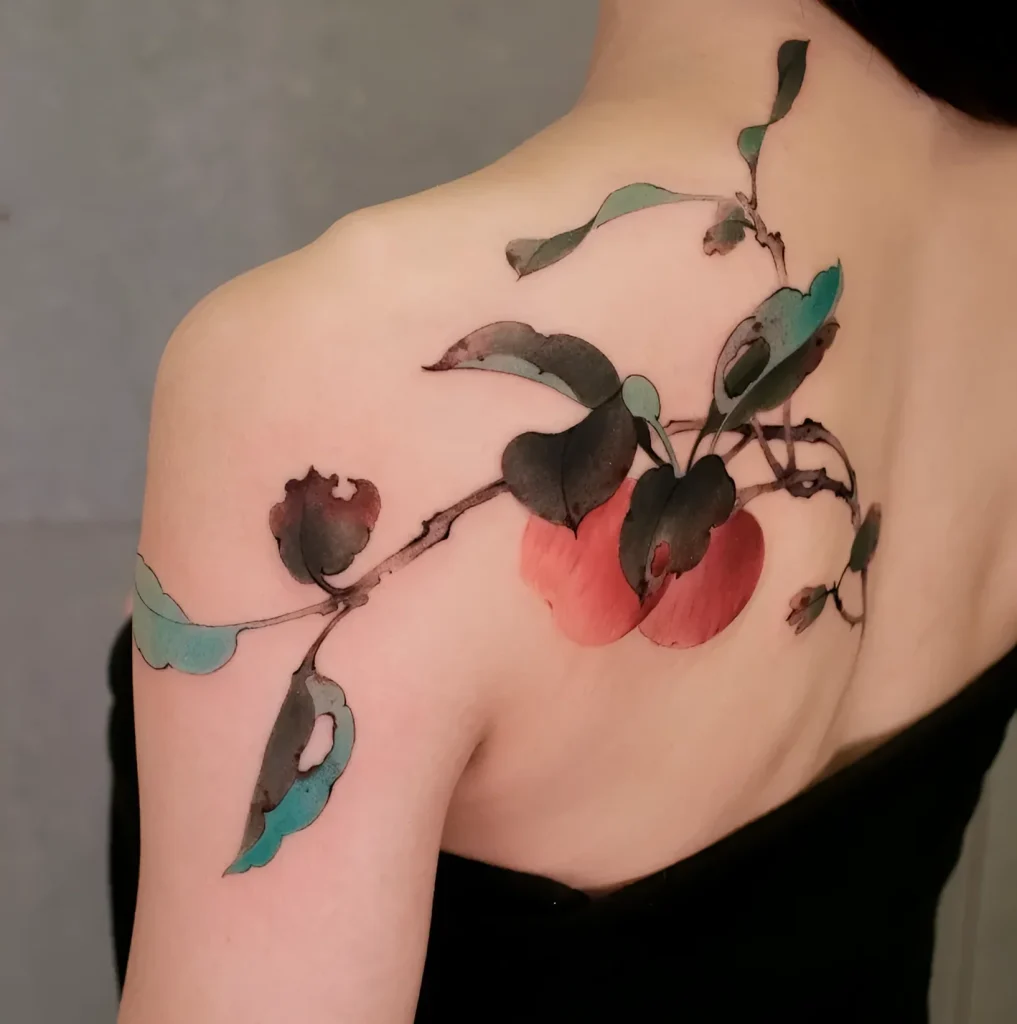 Watercolor tattoo of an apple branch with red fruits on a woman's shoulder blade, done in soft tones.