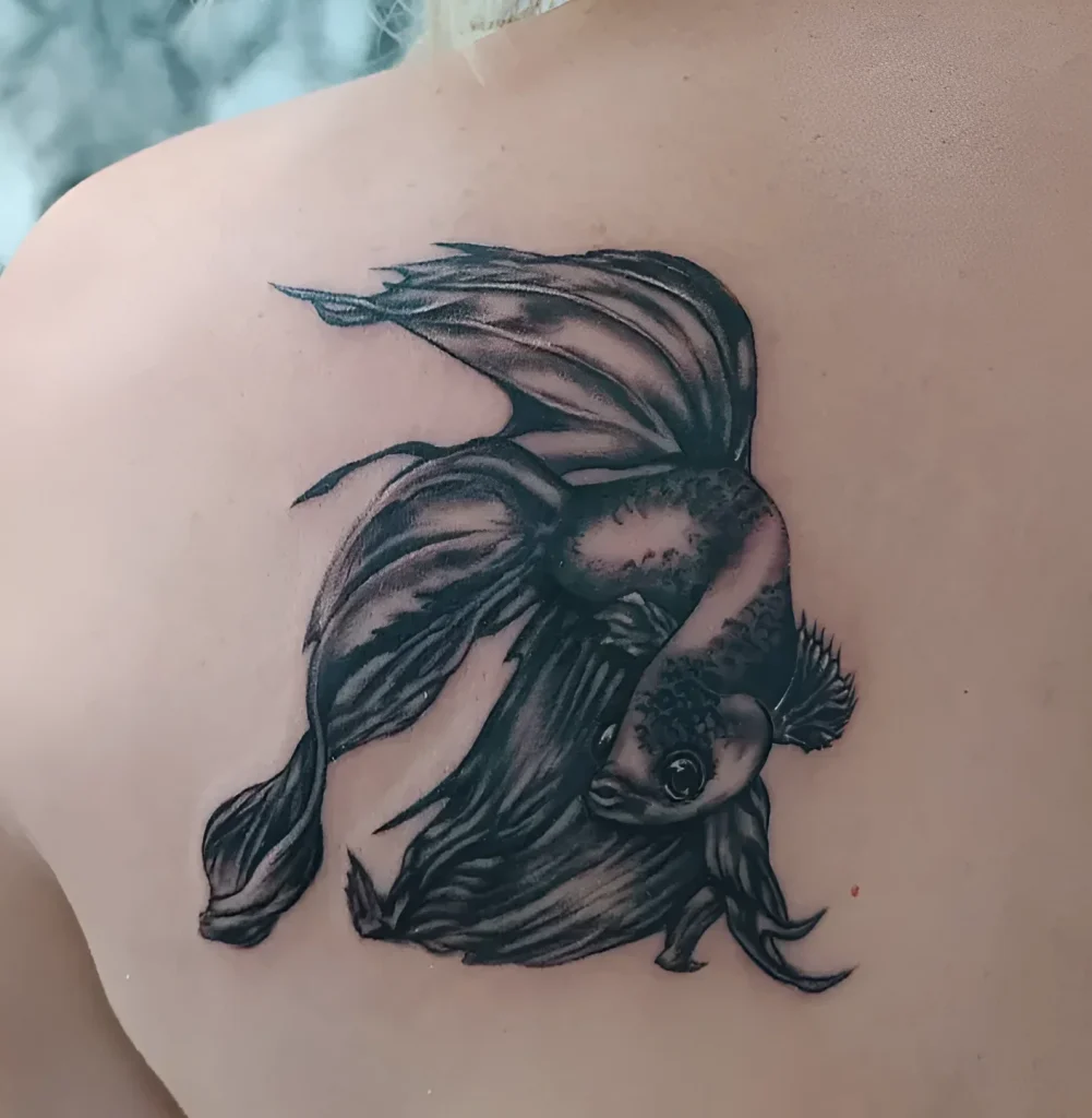 Black and grey realistic fish tattoo on the shoulder blade, fins spread, looking down.