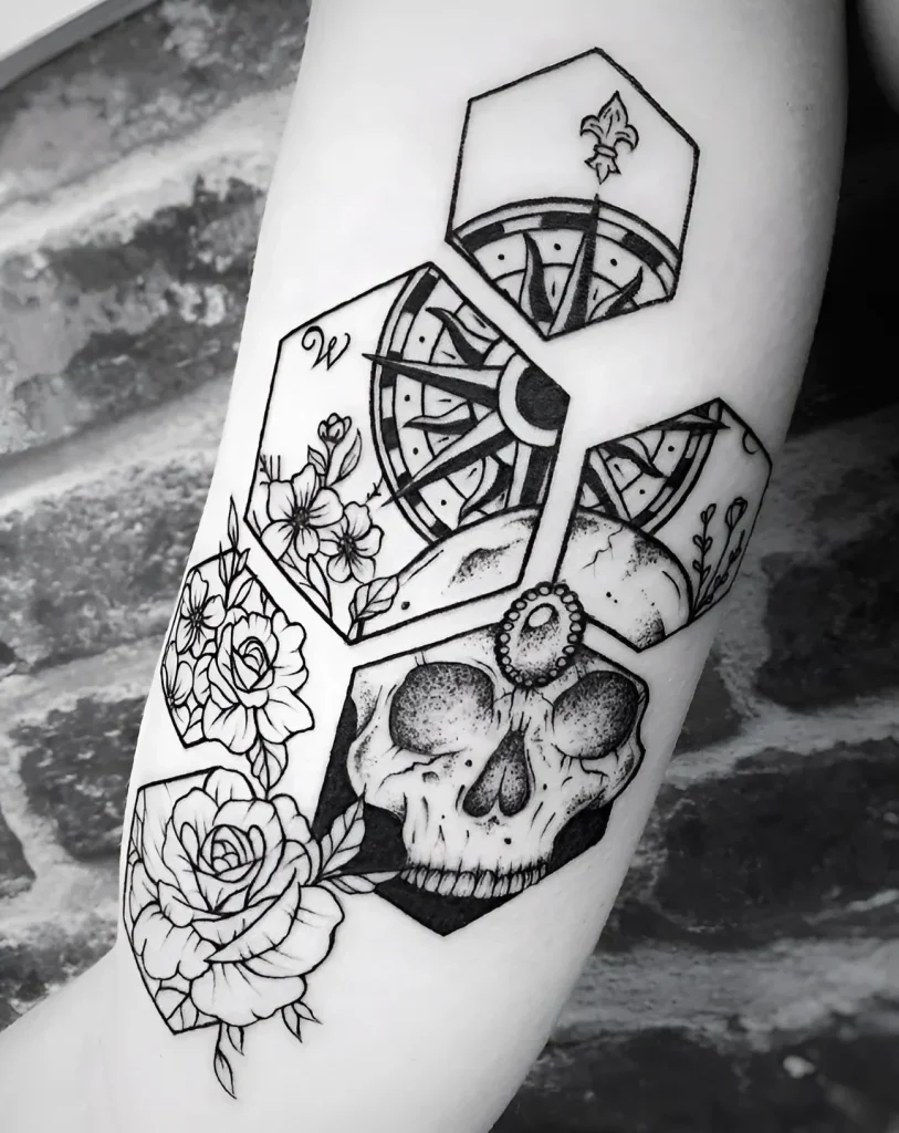 Tatouage noir et blanc sur le biceps représentant une boussole, un crâne et des roses, inscrits dans des figures géométriques, réalisé dans un style graphique.