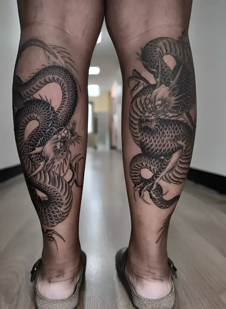 Black and white dragon tattoo wrapping around both calves, detailed scales and face, Japanese style.