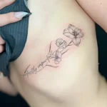 Черно-белая татуировка мака с надписью 'perfectly imperfect' на боковой части грудной клетки девушки