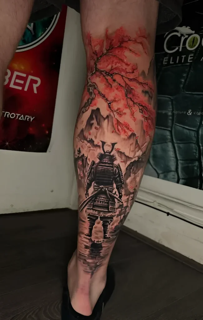 Photo of a calf tattoo: samurai in armor against a backdrop of blooming sakura and mountains, done in realism with watercolor elements.